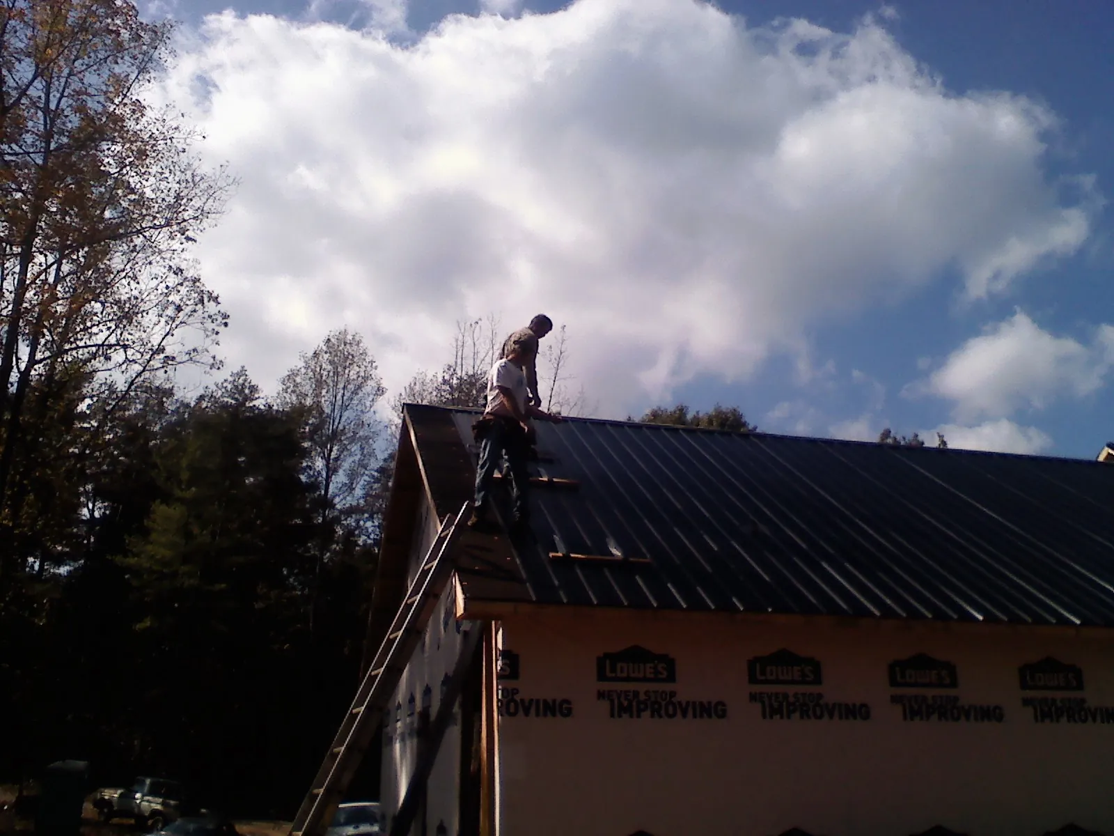 Roofer fastening dark metal panels high against a cloudy sky, from a Roof Inspection job in Oakfield